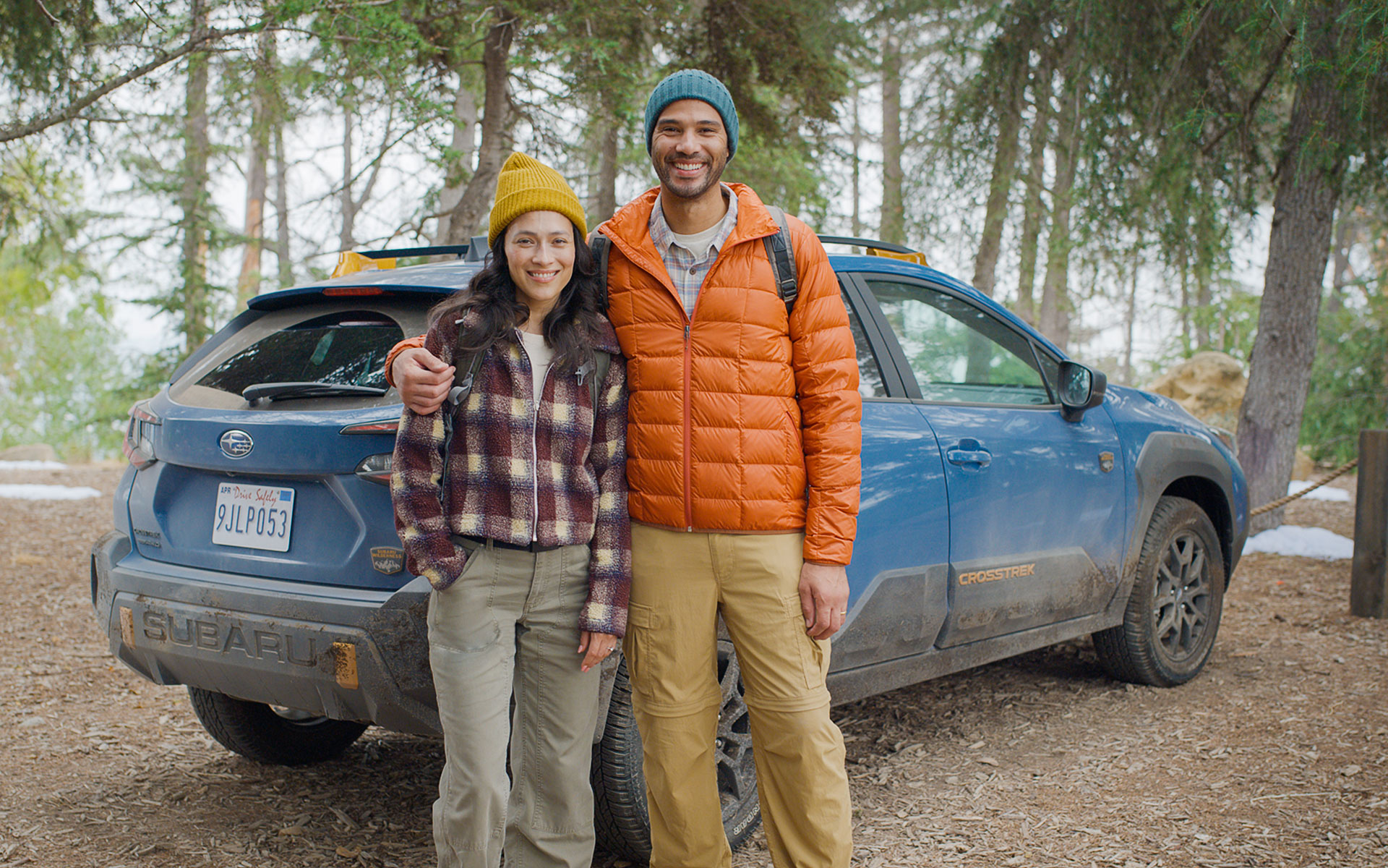 Couple standing in front of a Subaru Crosstrek Wilderness in wooded landscape.