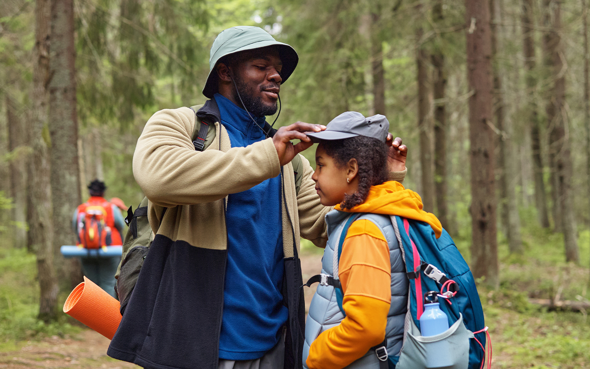 Dad putting hat on daughter in a wooded setting.