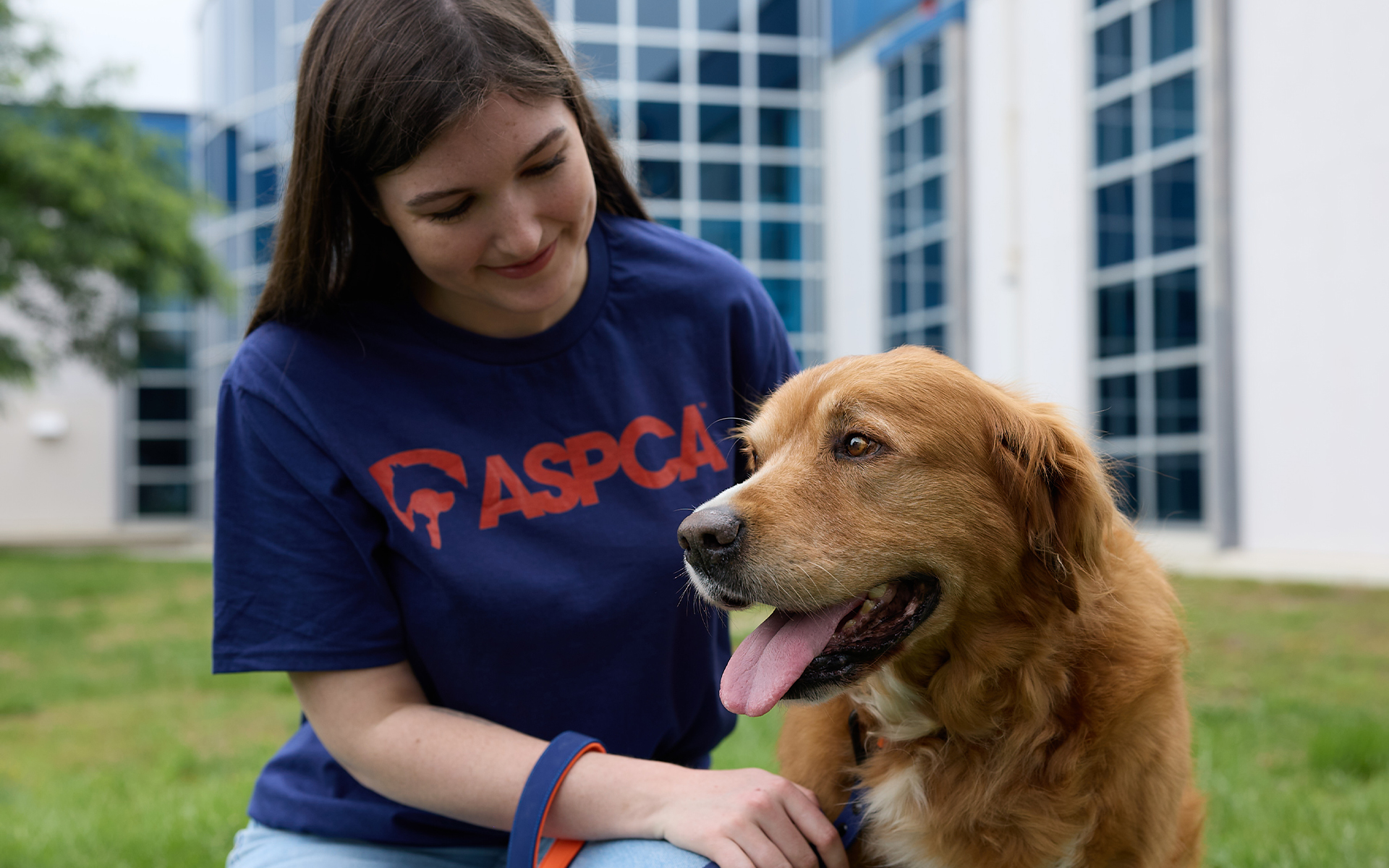 Woman in ASPCA shirt sitting and smiling at dog.