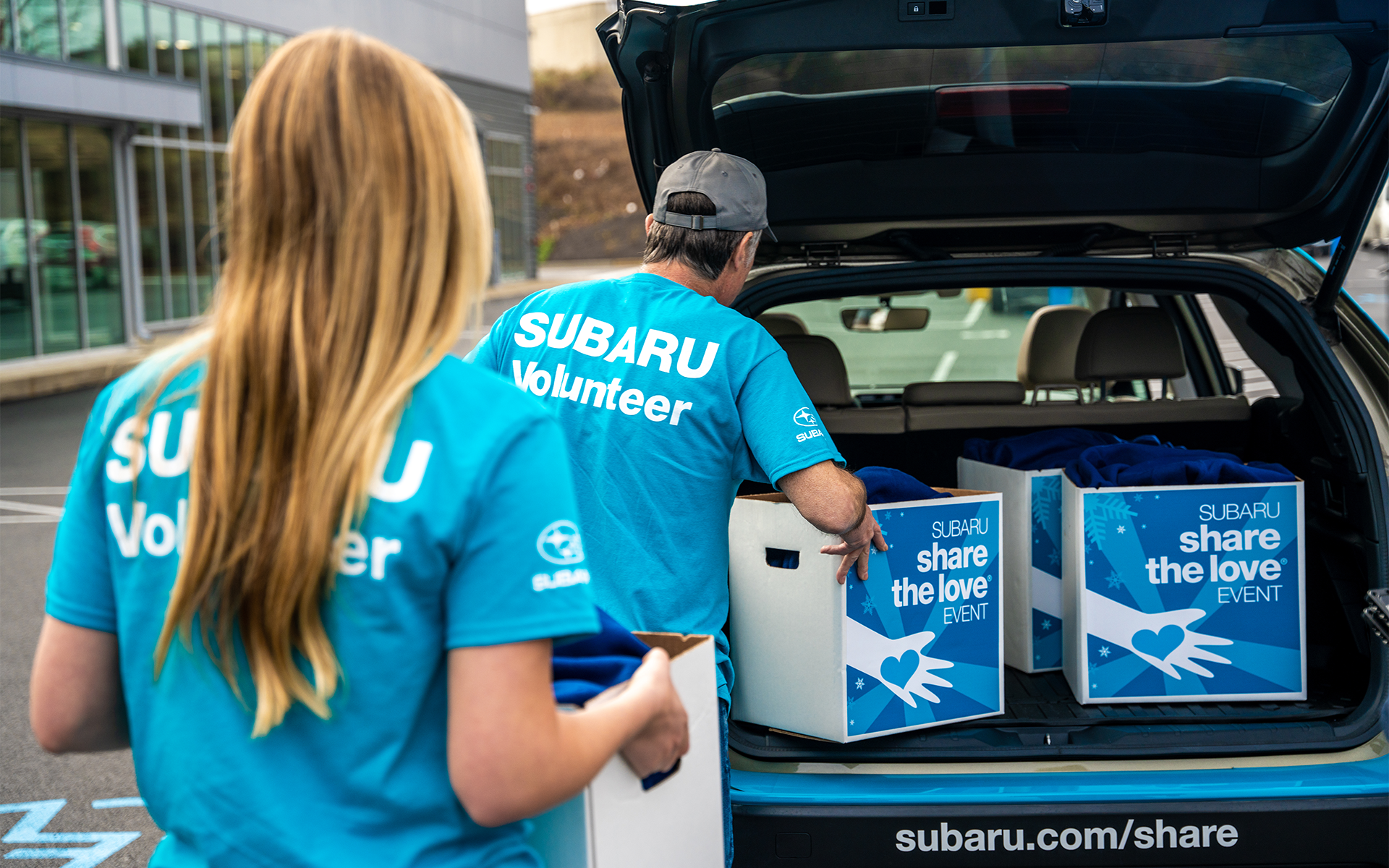 Two Subaru volunteers packing a vehicle with Subaru Share the Love Event boxes of donations.